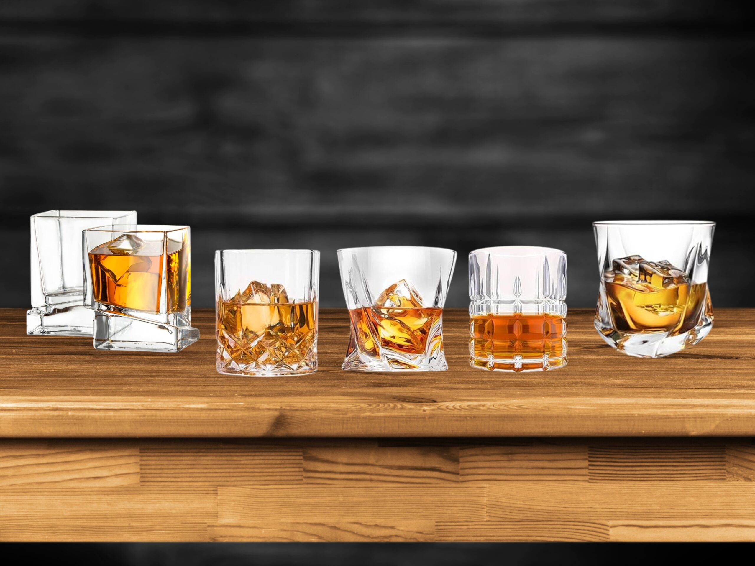 A variety of whiskey glasses—Glencairn, rocks, and lowball—filled with whiskey on a wooden bar counter.